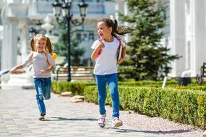 two school girls wearing backpack outside the primary school. schoolgirl, elementary school student going from school, graduation, summer holidays. photo