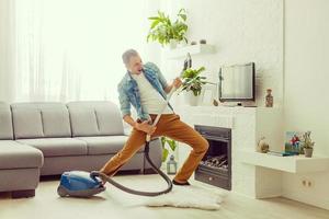 Young man having fun cleaning house with vacuum cleaner dancing like guitarist photo