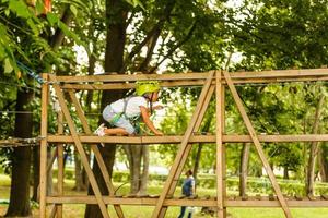 Little girl is standing on a rope, holding a rope with his hands. A child in a rope park passes obstacles photo