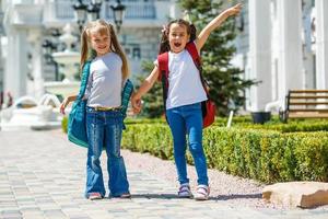 two school girls wearing backpack outside the primary school. schoolgirl, elementary school student going from school, graduation, summer holidays. photo