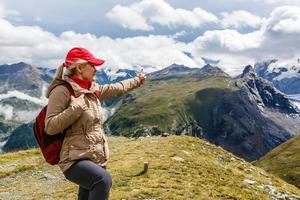 Young happy woman with backpack standing on a rock and looking to a valley below photo