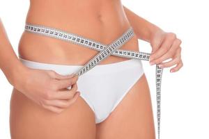 fit young woman measuring her waistline, white background photo