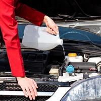 Cropped image of woman pouring windshield washer fluid into car photo