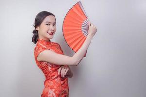 mujer asiática con vestido nacional del año nuevo chino sosteniendo un abanico de madera roja y sonriendo en un fondo suave y aislado, celebrada en la atractiva cultura de china foto