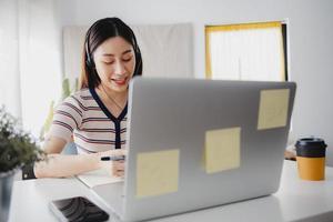 hermosa maestra asiática o linda estudiante enseña y aprende en línea en una computadora portátil en casa foto