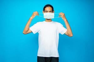 Asian Thai man wearing face mask to protect flu and Coronavirus or Covid-19 on blue background in studio