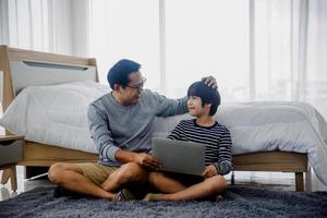 papá o padre habla con su hijo trabajando en una laptop en la habitación de la cama, tiempo familiar y concepto de amor de comunicación foto