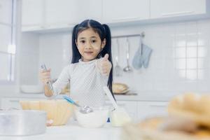 niña asiática feliz y divertida aprendiendo a cocinar dulces o panadería y mostrar el golpe