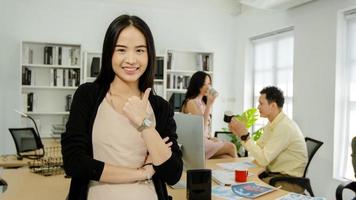 retrato de una hermosa mujer de negocios asiática en ropa casual mostrando el pulgar hacia arriba como freno y relajación en la oficina foto