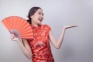 mujer asiática con vestido nacional del año nuevo chino sosteniendo un abanico de madera roja con una sonrisa y mostrando la mano para presentar y su producto en un fondo suave y aislado, celebrado en la atractiva cultura de china