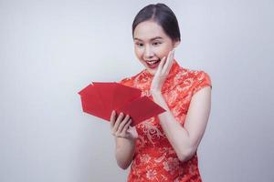 mujer asiática con vestido nacional del año nuevo chino sosteniendo un ang pao rojo de bolsillo de dinero con una gran sonrisa en un fondo suave y aislado, celebrada en la atractiva cultura de china foto