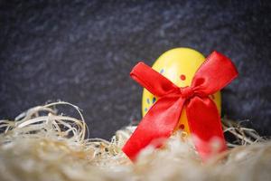 Yellow easter eggs with red ribbon bow in the nest on dark background photo