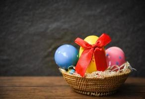 huevos de Pascua con lazo de cinta roja en la cesta del nido sobre una mesa rústica de madera y fondo oscuro foto