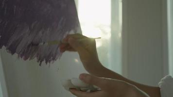 stänga upp hand professionell konstnär använda sig av paintbrush i abstrakt konst för skapa mästerverk. målare måla med akvareller eller olja i studio hus. kvinna njut av målning som hobby. arbete rekreation video