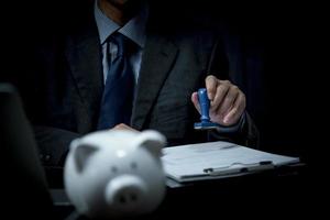 Businessperson is stamping a rubber stamp on a financial and banking approval document or paper contract agreement on desk. photo