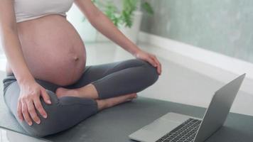 gravid kvinna är spelar yoga förbi ser tittar på bärbar dator. yoga till minskar de svaghet av de muskler. begrepp hälsa för gravid kvinnor. video