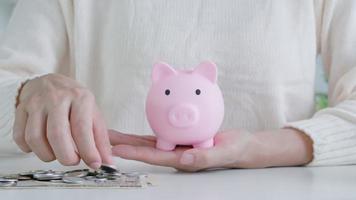 closeup of business woman hand putting money coin into piggy bank for saving money. wealth, Finance, business, investment, retirement, future, accounting, plan life, economize, conserve, family video