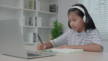 curso en línea de formación y aprendizaje para niños asiáticos. videoconferencia en la computadora portátil en casa. Reproduzca el curso en línea, las estudiantes usan auriculares para estudiar, anotan la tarea, clases de video, nueva educación.