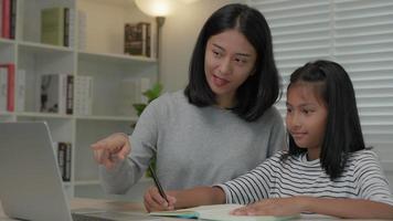 asiatico giovane poco ragazza imparare a casa. fare compiti a casa con genere madre aiuto, insegnare e incoraggiare per esame. ragazza contento su scuola a casa. mamma insegnare e consigli formazione scolastica in linea. video