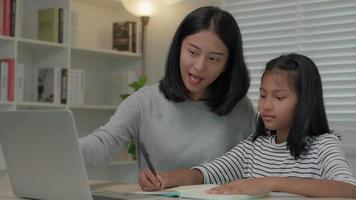 mutterunterricht für tochter per laptop. asiatische junge kleine Mädchen lernen zu Hause. Hausaufgaben mit freundlicher Mutterhilfe machen, zur Prüfung ermutigen. Asien Mädchen glücklich Homeschool. Mutter rät Bildung zusammen.