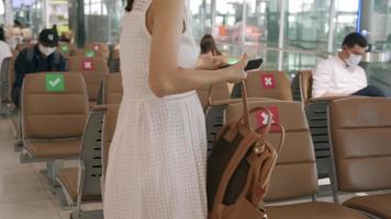 concepto de distancia social. mujer asiática con una máscara esperando un avión en el aeropuerto. usar una máscara en lugares públicos previene la propagación del virus tanto para usted como para los demás video