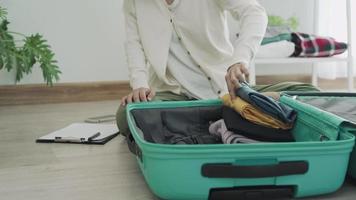 uma mulher dobra as roupas e as coloca na bolsa para se preparar para uma viagem. uma mulher prepara suas malas para sua viagem de trabalho e usa a lista de verificação para verificação cruzada. video