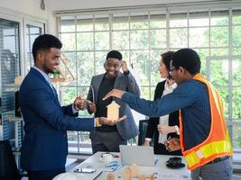 los colegas multirraciales de los empresarios intercambian ideas con modelos de casas y planos en la oficina. equipo de construcción profesional discutiendo la disposición de las líneas de servicio en el nuevo edificio. foto