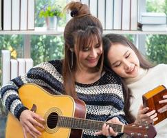 Young Asian lesbian couple intending to play a musical instrument together, guitar and kalimba, in the living room at home, the lifestyle of couple LGBT loving women happy in romantic love and fun photo