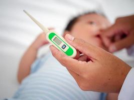 Baby illness medicine flu fever and thermometer, a doctor checks the temperature of the ill baby. Digital thermometer to measure the heat temperature of a sick child. Baby fever concept photo