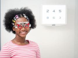 African girl putting optical trial frame to determine visual acuity. health care, medicine, people, eyesight and technology concept photo