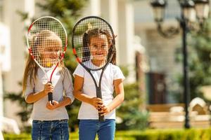 Happy preteen girls in sport outfits with tennis rackets on green grass background photo