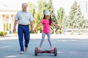 Little smiling girl learning to ride a hoverboard with her parents outdoors photo