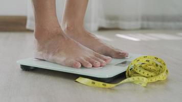 Woman foot stepping on weigh scales with tape measure. A woman is weighing herself after eating food. Woman serious about weight because need diet. Diet Concept and loss weight.