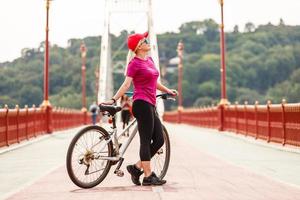 hermosa chica con cabello rubio felizmente montando en bicicleta. retrato de una joven con gafas de sol j divirtiéndose, montando en bicicleta por las calles de la ciudad foto