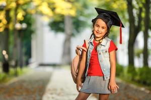 Happy school kid graduate in graduation cap looking up photo