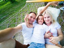 family laying down and relaxing together on a hammock during a sunny summer day on holiday home garden. Family relaxing outdoors, healthy and wellness lifestyle. photo