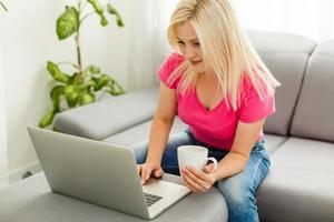 Happy young woman is relaxing on comfortable couch and using laptop at home. Photo toned.