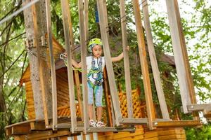 Niña de la escuela feliz disfrutando de la actividad en un parque de aventura de escalada en un día de verano foto