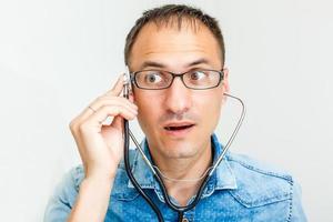 Portrait of young cheerful male doctor in uniform with phonendoscope over white background photo