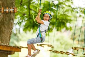 adorable niña disfrutando de su tiempo en el parque de aventuras de escalada en un cálido y soleado día de verano. actividades de verano para niños pequeños. niño divirtiéndose en vacaciones escolares. foto