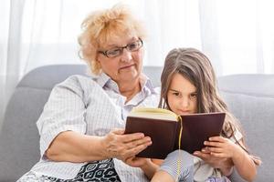 Grandmother And Granddaughter Reading Book On Garden Seat photo