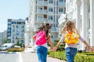 two school girls wearing backpack outside the primary school. schoolgirl, elementary school student going from school, graduation, summer holidays. photo