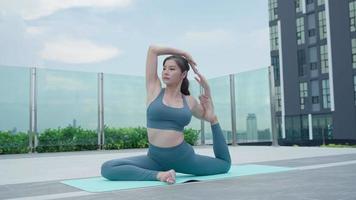 schlanke Frau, die Yoga auf dem Balkon ihrer Eigentumswohnung praktiziert. asiatische frau, die morgens übungen macht. balance, meditation, entspannung, ruhe, gute gesundheit, glücklich, entspannen, gesundes lebensstilkonzept