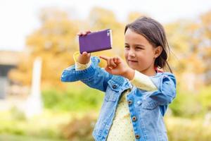 education, school, technology and internet concept - little student girl with smartphone in the park photo