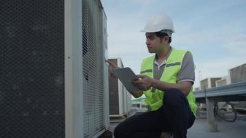 un ingénieur de maintenance asiatique travaille sur le toit de l'usine. le superviseur inspecte le système de compresseur et planifie l'installation de systèmes de climatisation sur le chantier de construction de bâtiments modernes. video