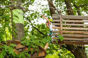 Little girl is standing on a rope, holding a rope with his hands. A child in a rope park passes obstacles photo