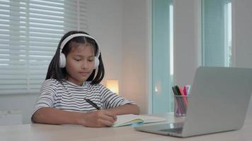 curso de tutor en línea para niños asiáticos. videoconferencia en la computadora portátil en casa. Reproduzca el curso en línea, las estudiantes usan auriculares para estudiar, anotan la tarea, clases de video, nueva educación.