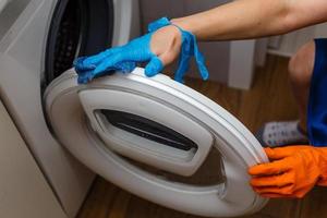mano en guante rasgado limpiando la lavadora. limpieza periódica. la criada limpia la casa. foto