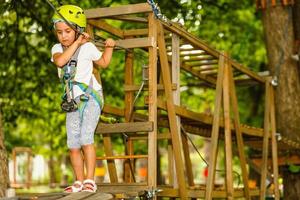 retrato de una niña sonriente con casco y arnés en el sendero en el parque de cuerdas del cielo en verano. foto