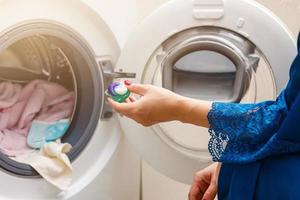 A close up of a young wife putting a cloth into washing machine photo